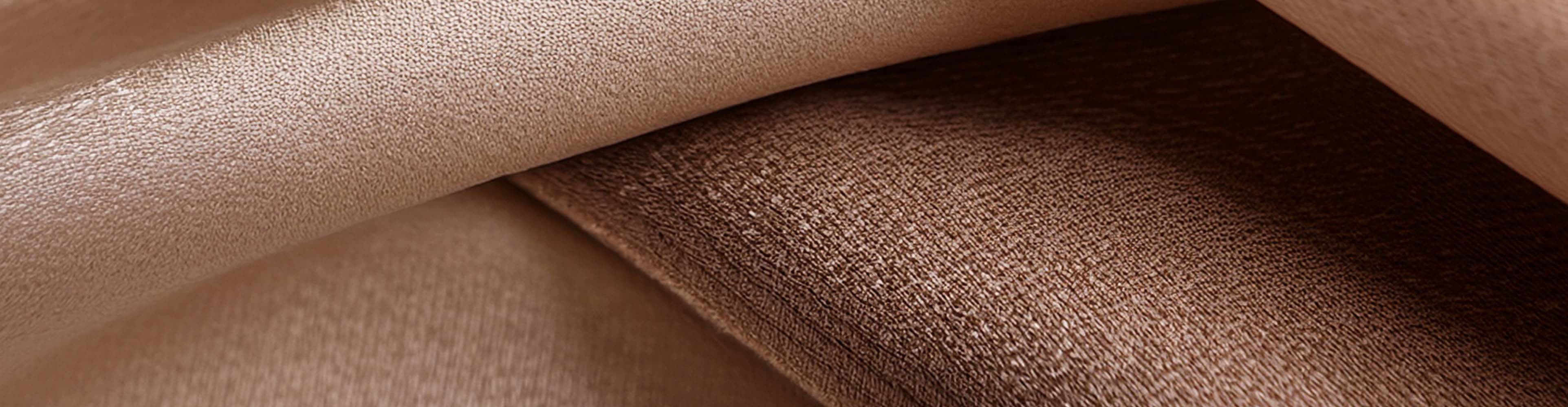 Nahaufnahme von weichem, glänzendem Stoff in warmen Beige- und Brauntönen.