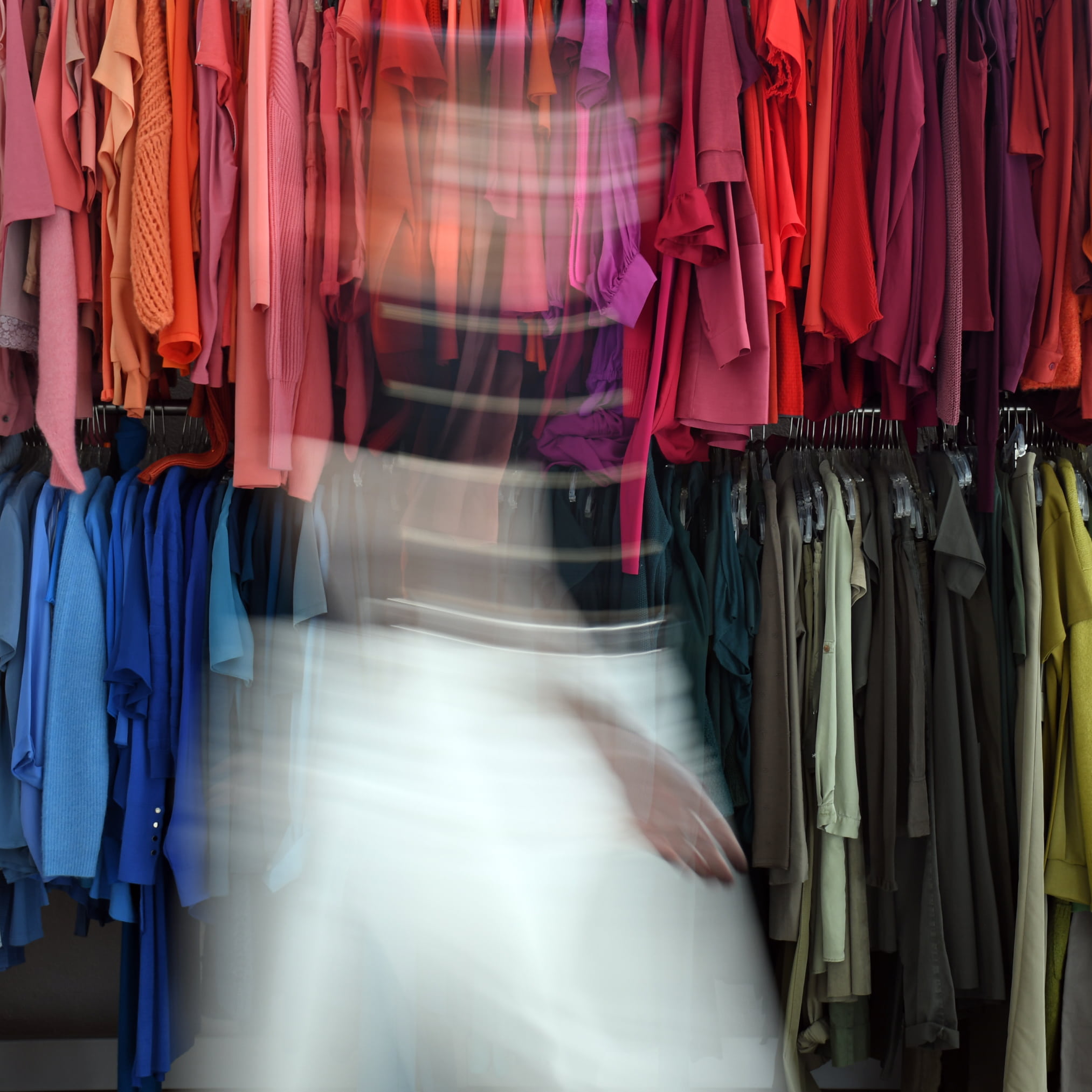 Person in Bewegung vor farblich sortierter Kleidung. 